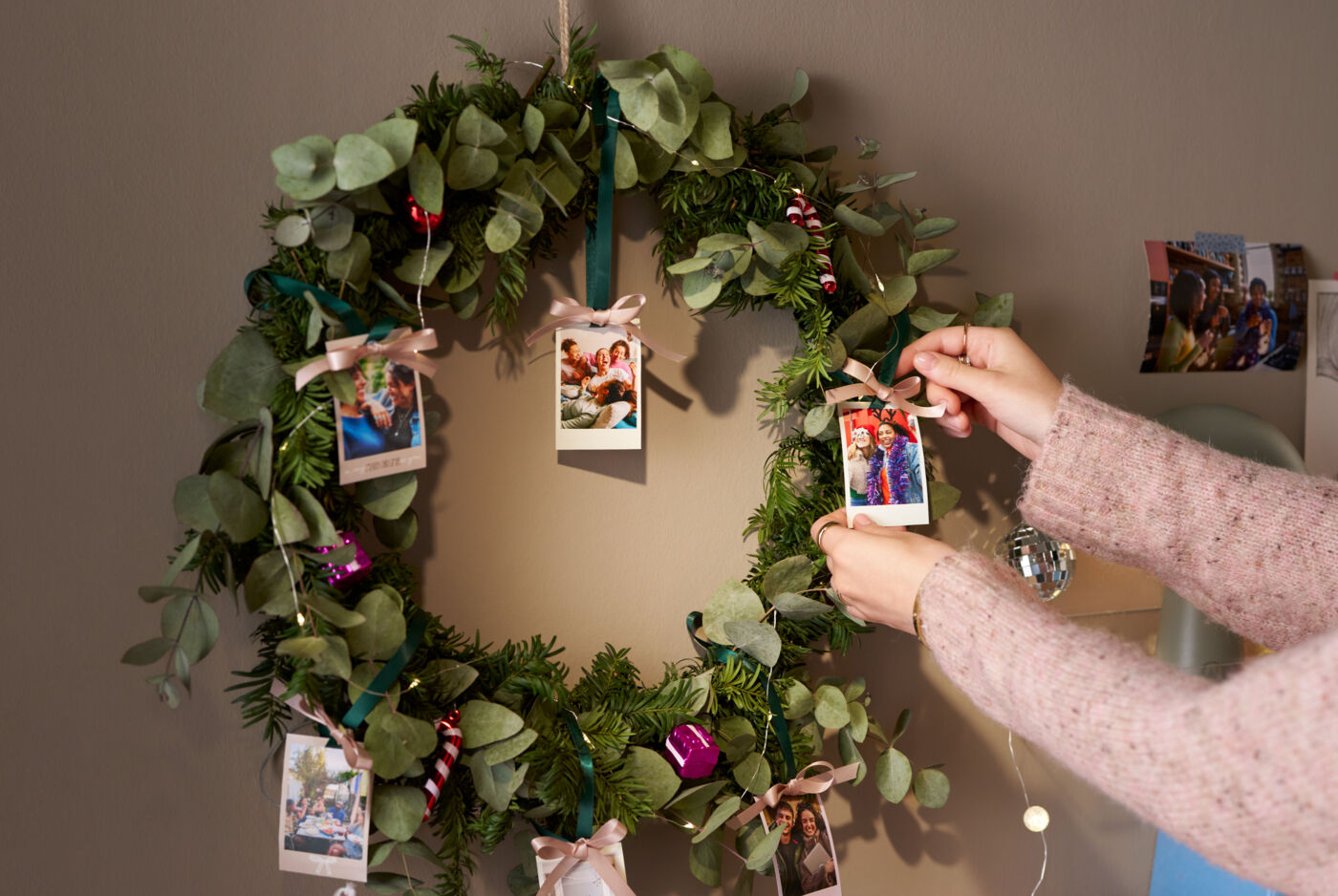Eine Frau dekoriert mit Fotoanhängern einen weihnachtlich geschmückten Kranz, der an einer Wand hängt.